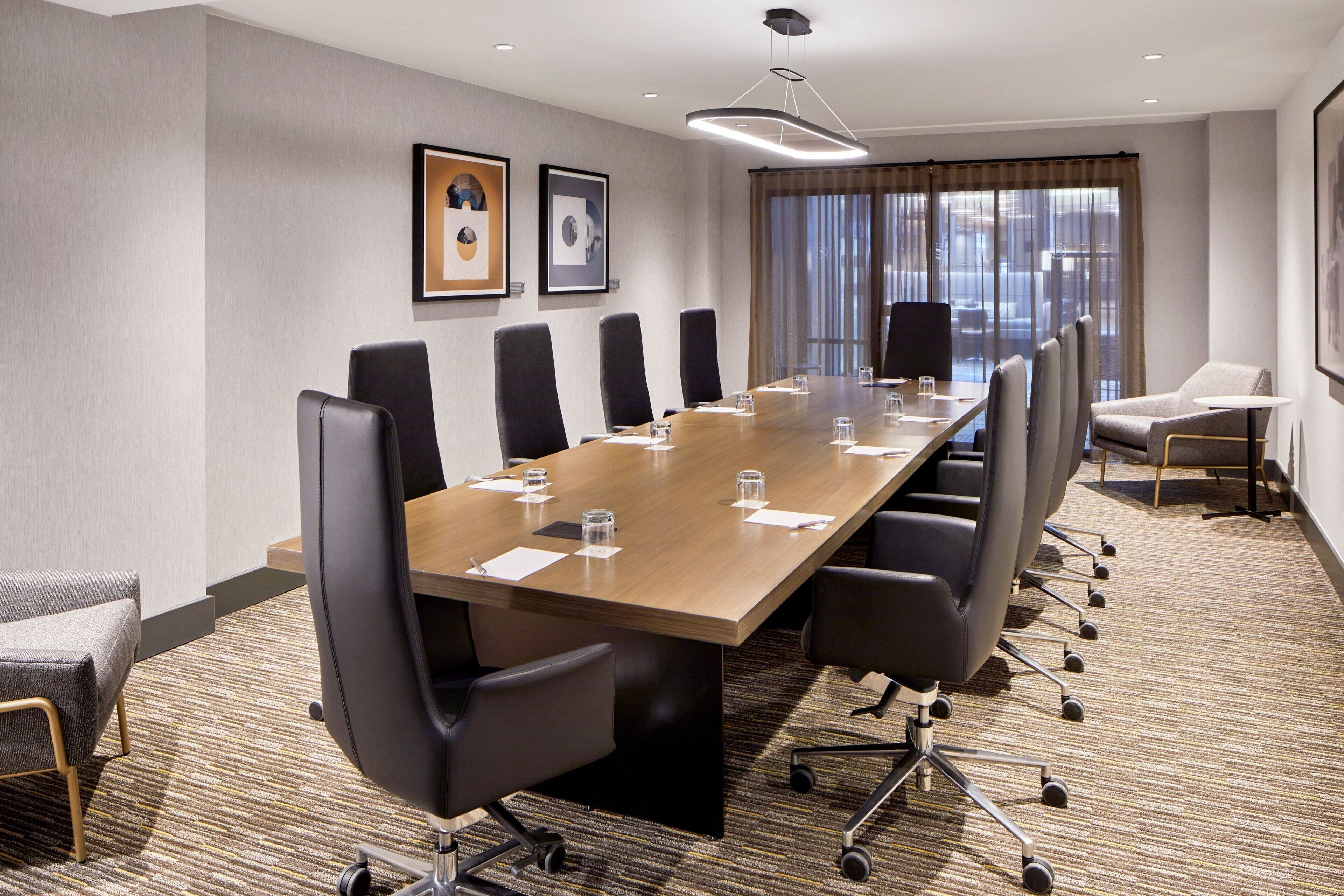 A conference room with a long table, multiple chairs, and a large window with curtains.