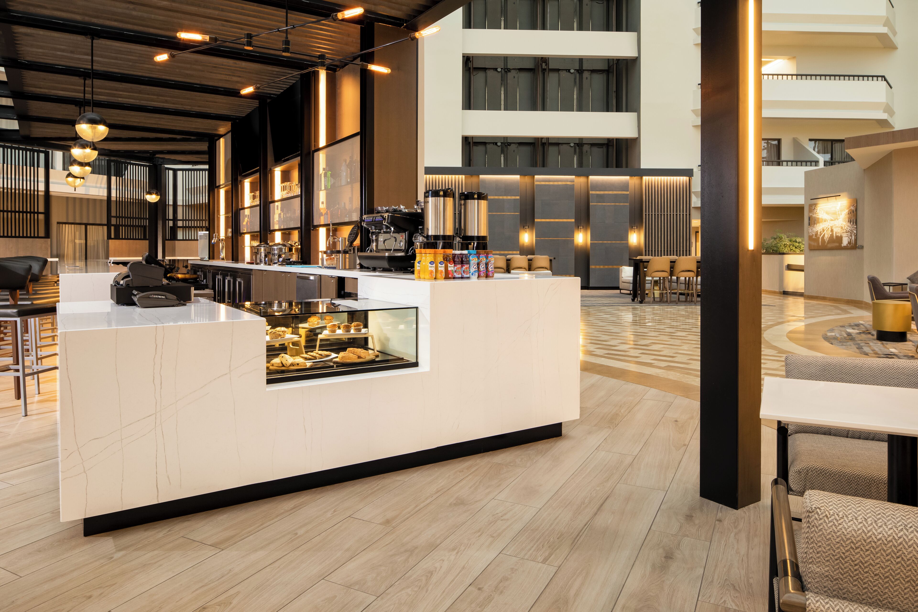 A modern hotel lobby with a central counter, seating area, and a staircase leading to upper floors.