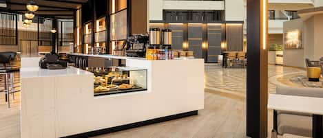 A modern hotel lobby with a central counter, seating area, and a staircase leading to upper floors.