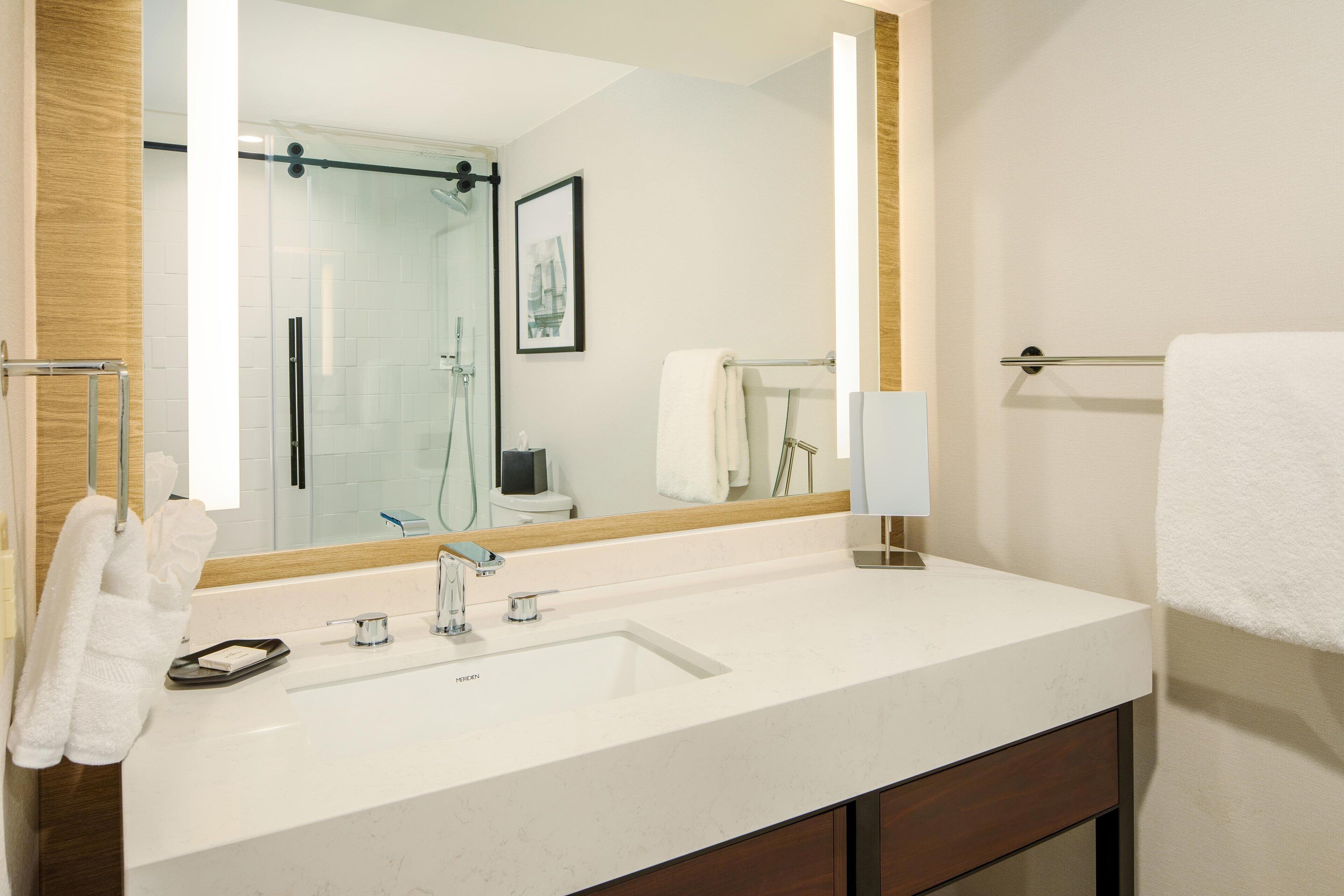 A modern bathroom with a large mirror, white sink, and wooden vanity.