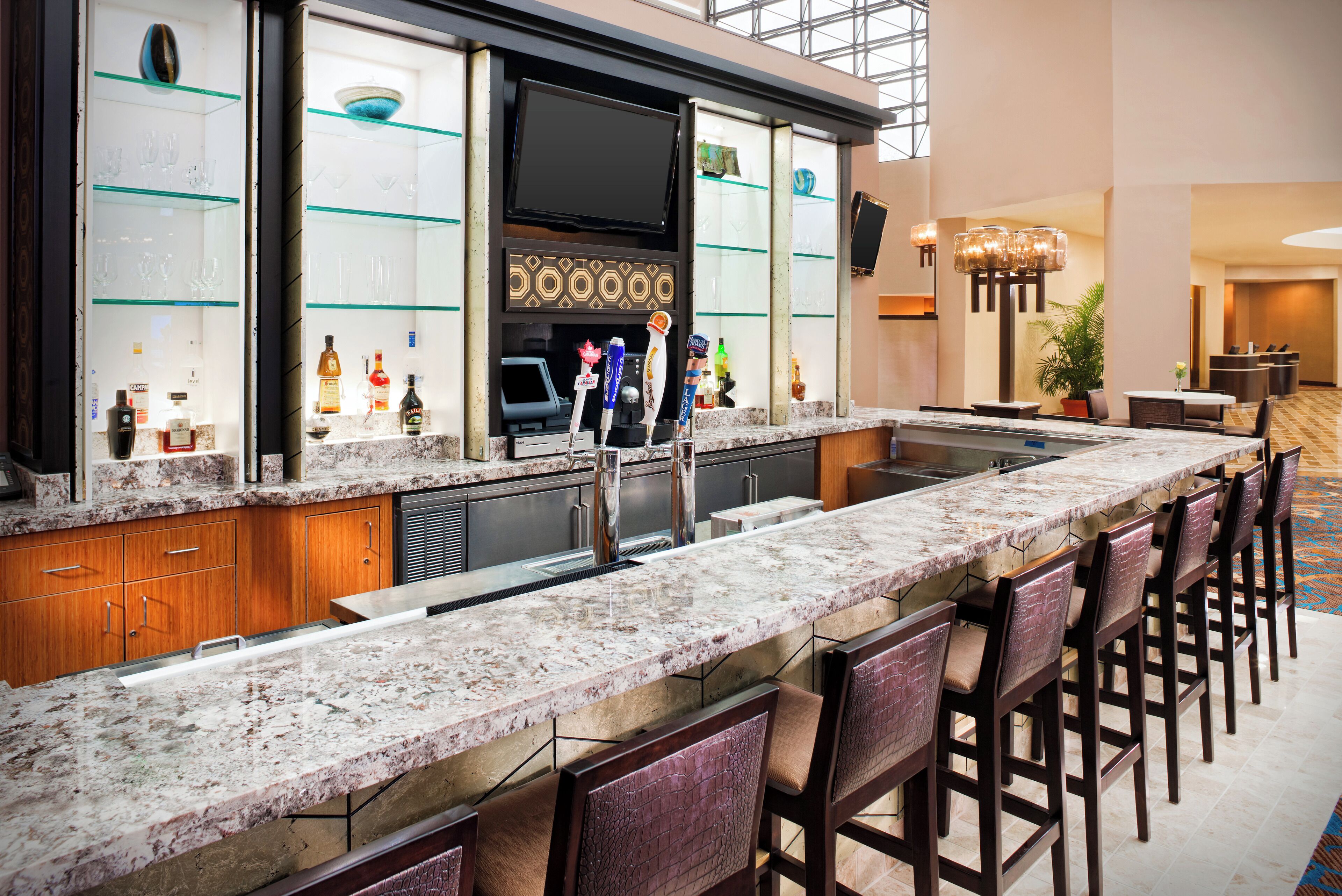 A modern bar area with a long counter, multiple stools, and a variety of bottles and glasses.