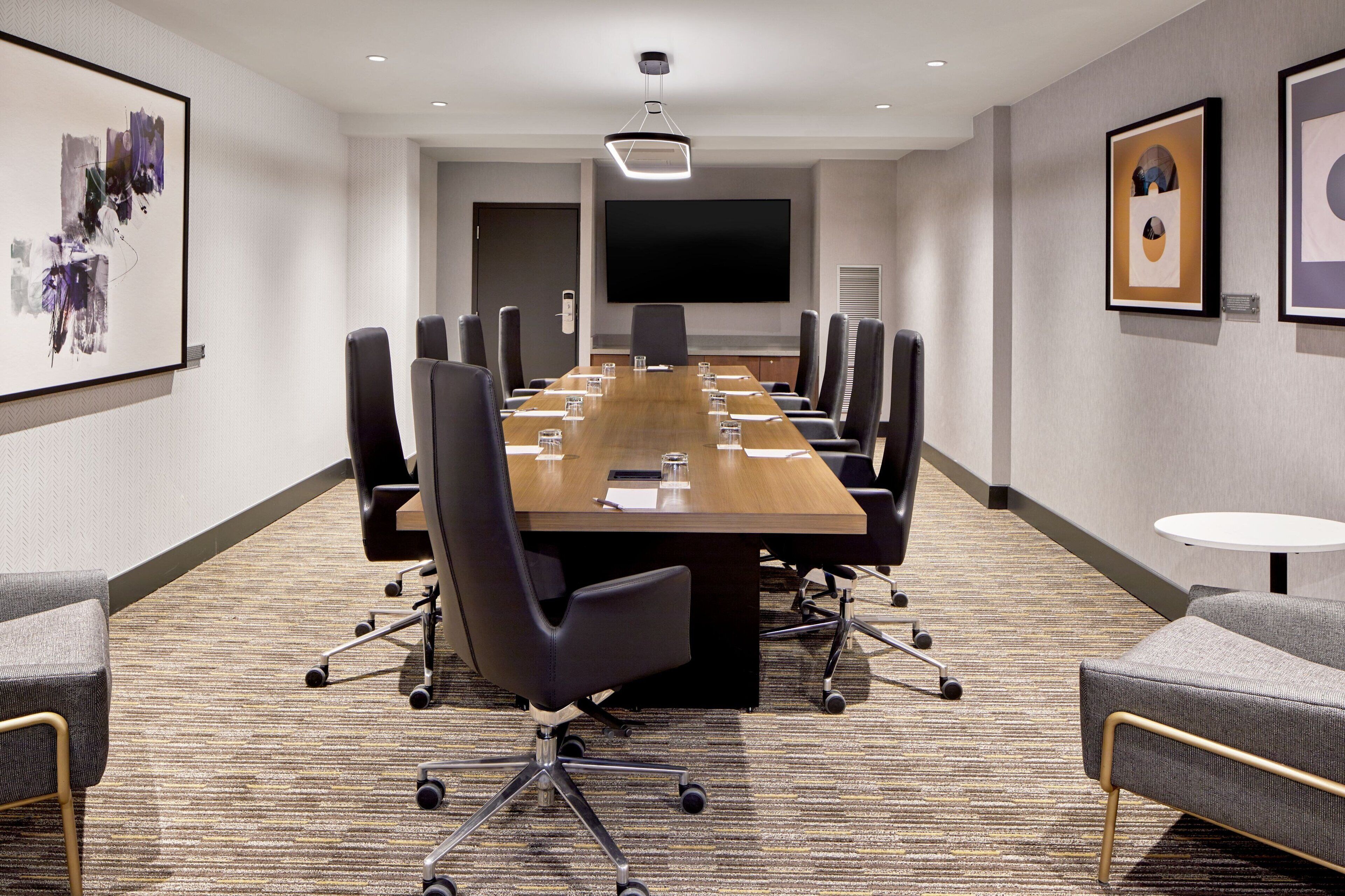 A conference room with a long table, chairs, a TV screen, and artwork on the walls.