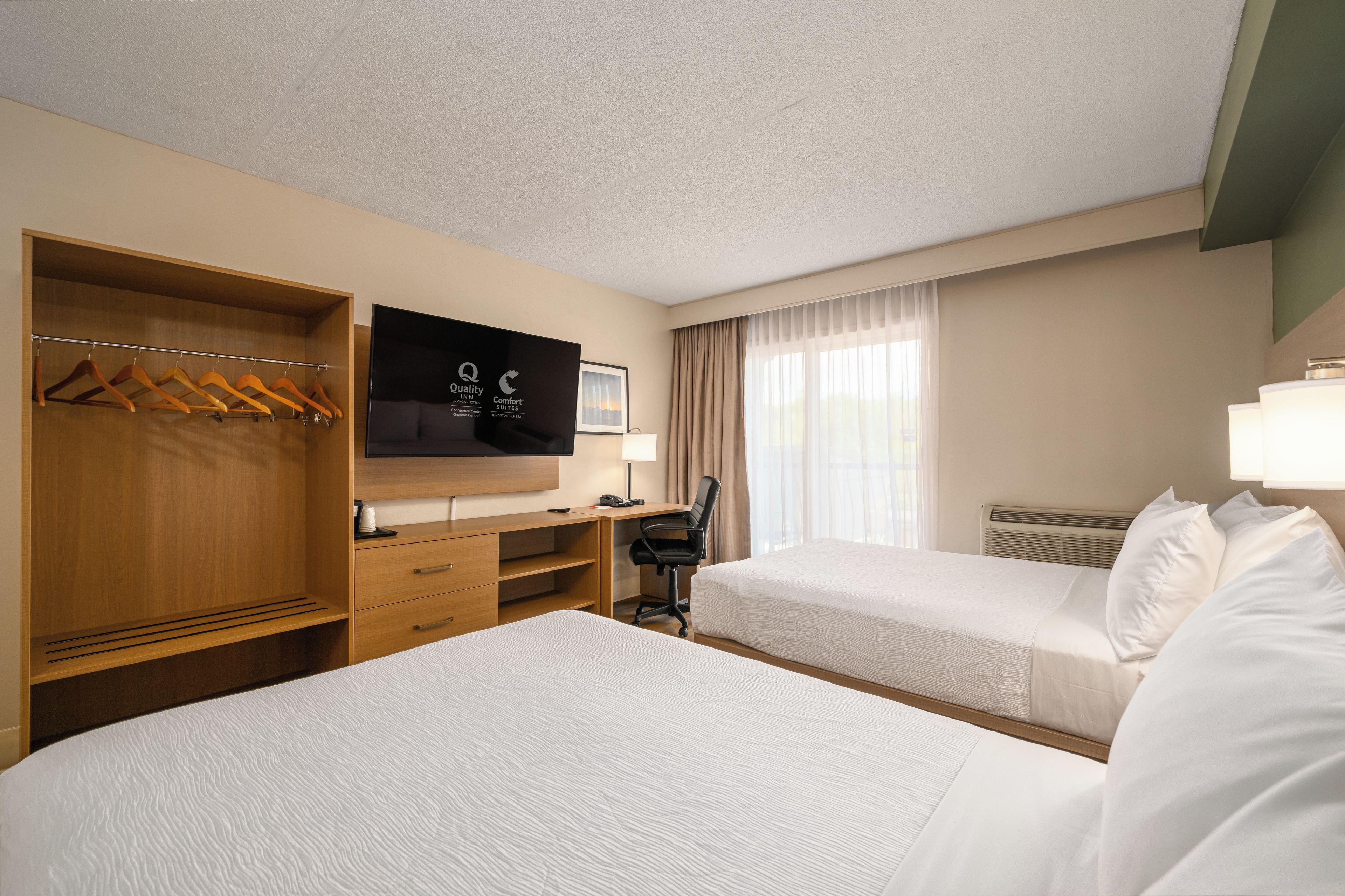 Habitación de hotel con dos camas, un escritorio, un televisor y un armario.
