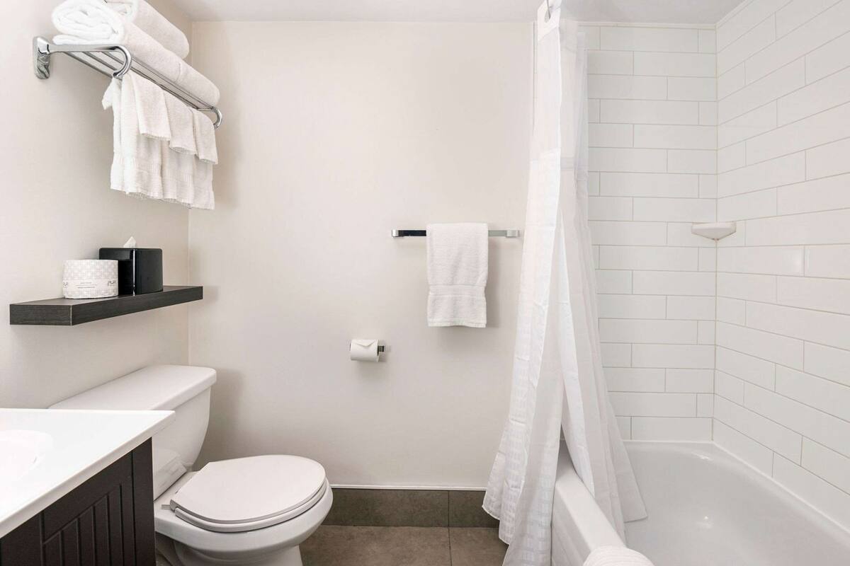 A bathroom with a toilet, a shower, and a bathtub. There are towels and toiletries on a shelf.