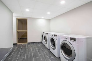 A laundry room with three front-loading washing machines, a wooden door, and a tiled floor. - Quality Inn & Conference Centre Kingston Central (Kingston)