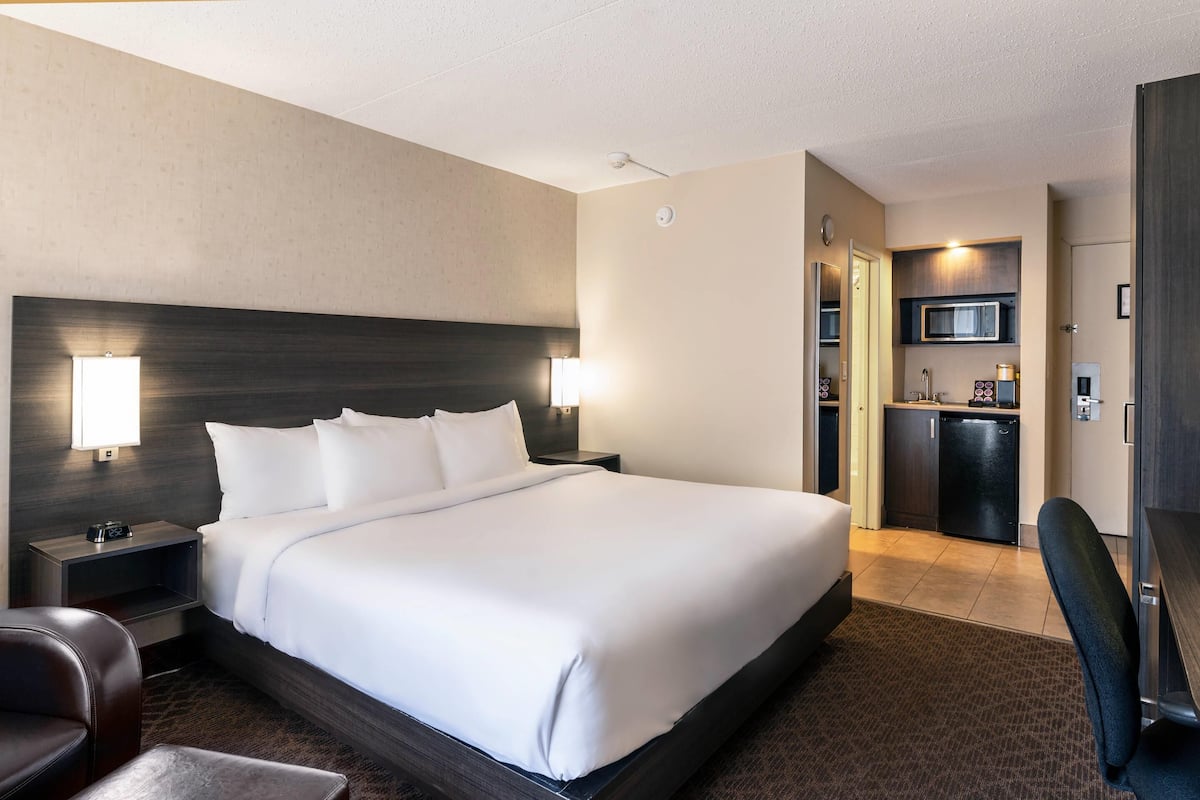 A hotel room with a large bed, bedside tables, a desk, a chair, and a kitchenette.