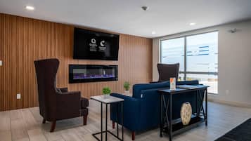 Una sala moderna con una televisión de pantalla plana, un sofá azul, un sillón oscuro, una mesita y un ventanal grande.