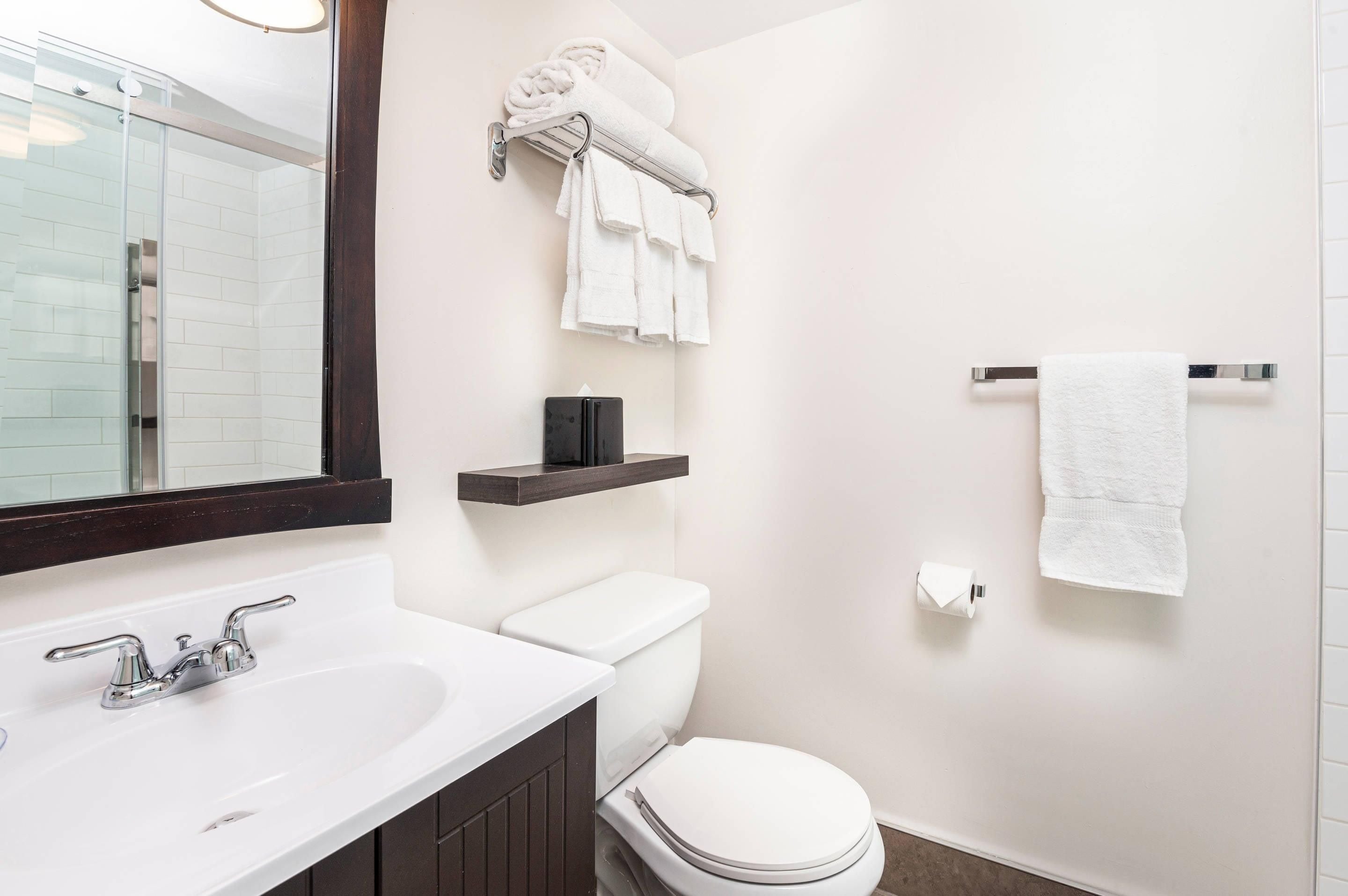 A bathroom with a white sink, a toilet, a towel rack with towels, and a mirror.