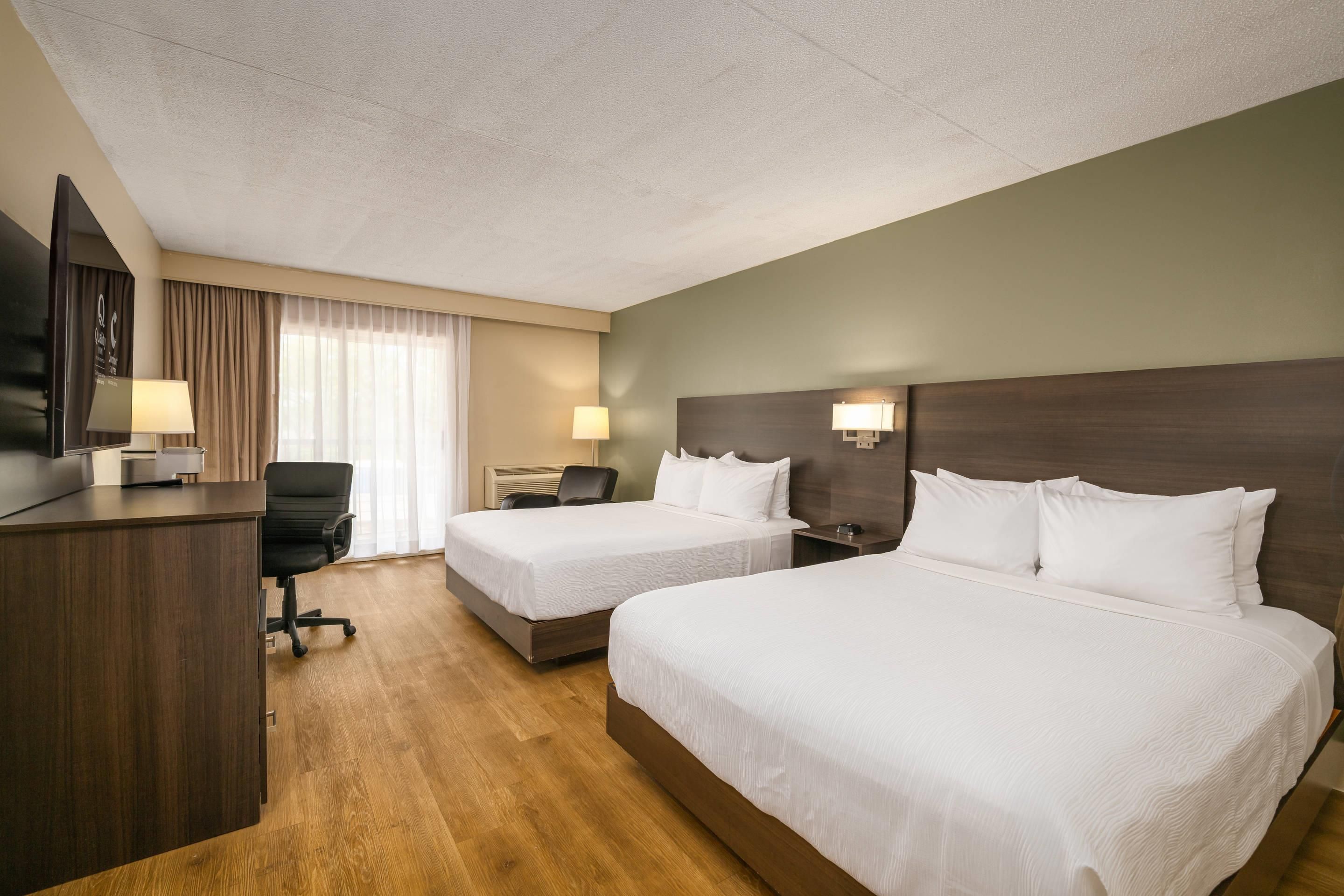 A hotel room with two beds, a desk, a chair, a TV, and a window with curtains.