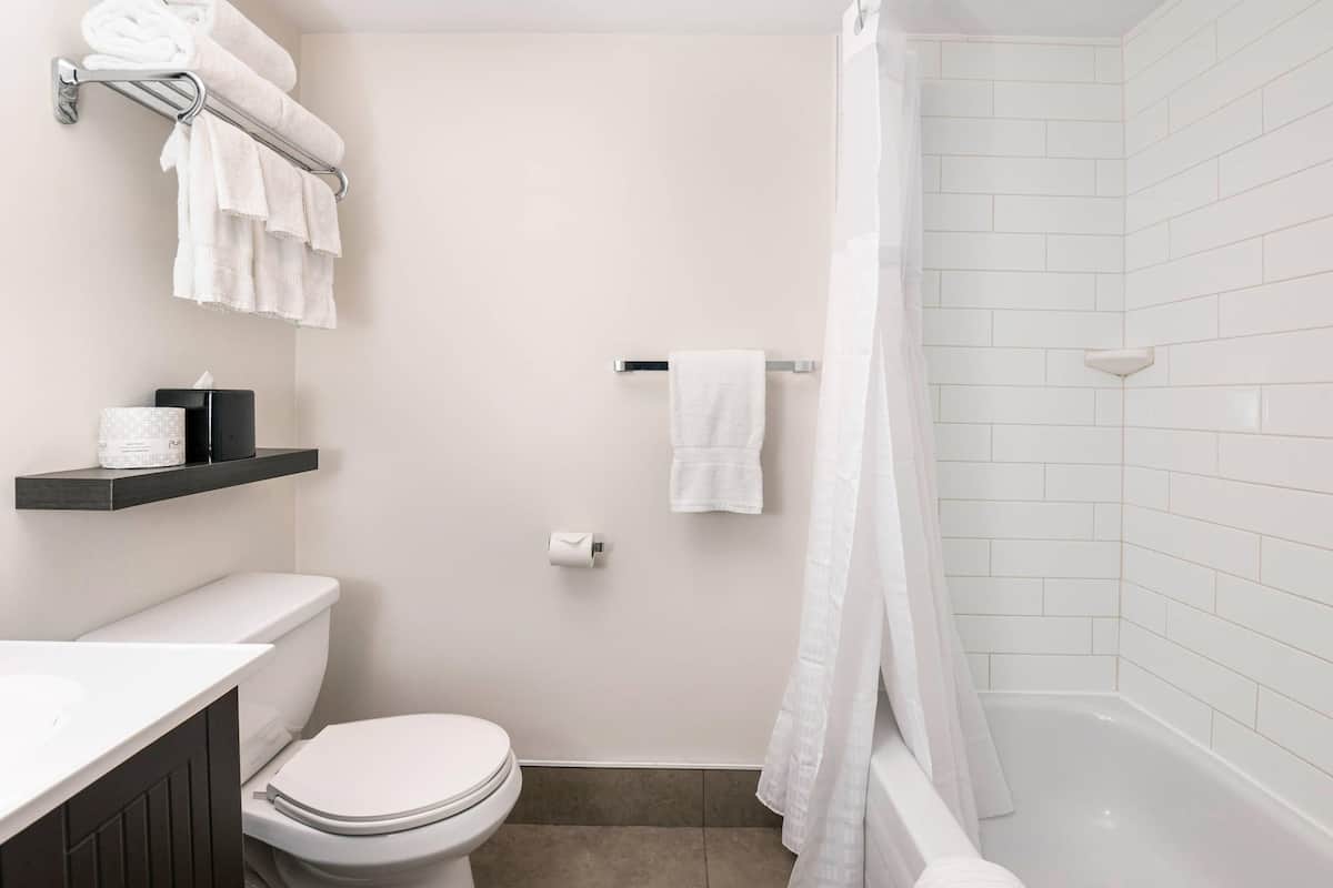 A bathroom with a toilet, a sink, a shower with a curtain, and a towel rack with towels.