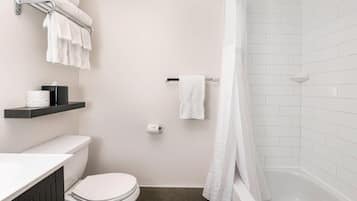Un baño pequeño y moderno con inodoro, ducha y bañera. Hay toallas y un rollo de papel higiénico en un estante.