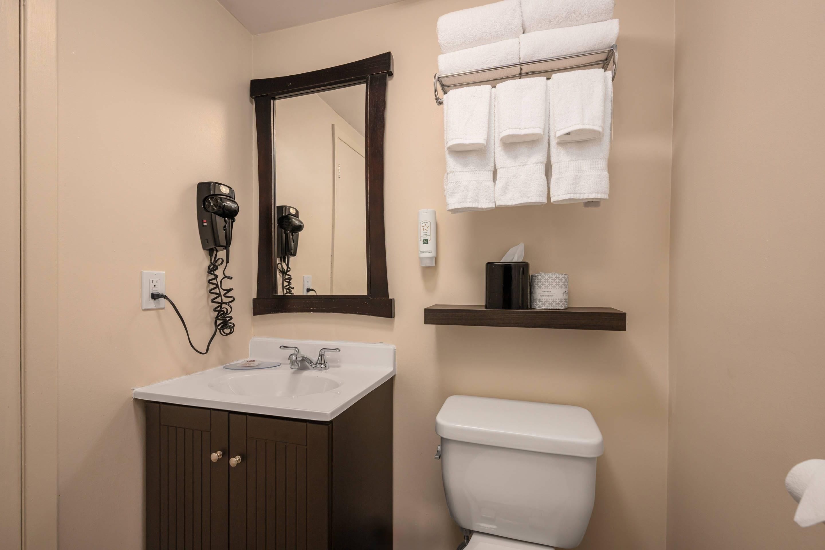 A bathroom with a white sink, a mirror, a hairdryer, a towel rack, and a toilet.