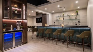 Un'area bar moderna con un bancone, sgabelli e una vetrina refrigerata.