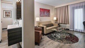 Una camera d'hotel moderna con un divano, un tavolino, una scrivania con uno specchio e un'ampia finestra con tende.