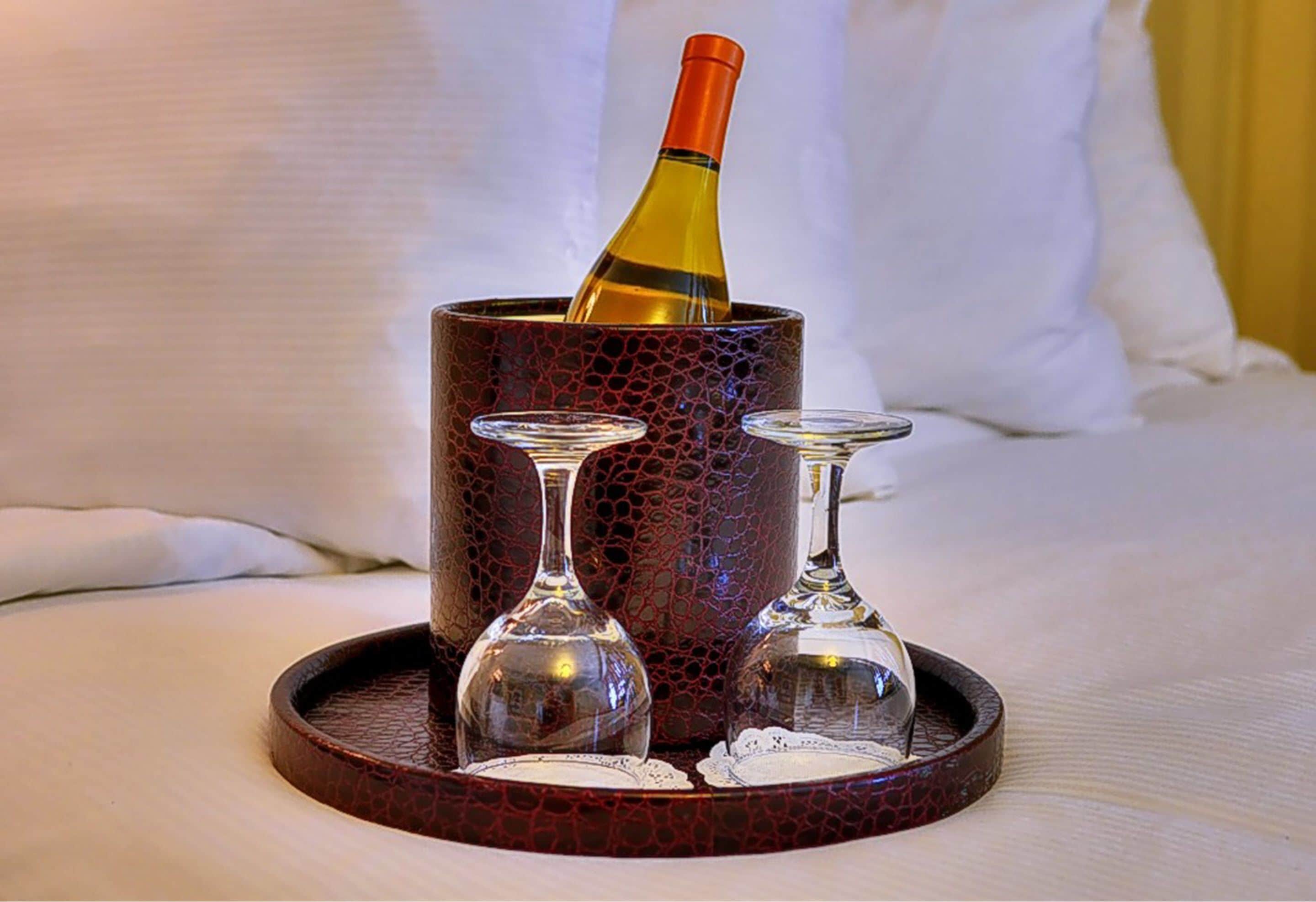 A bottle of wine in a textured container on a tray, with two empty wine glasses beside it.