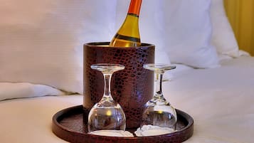 A bottle of wine in a textured container on a tray, with two empty wine glasses beside it.