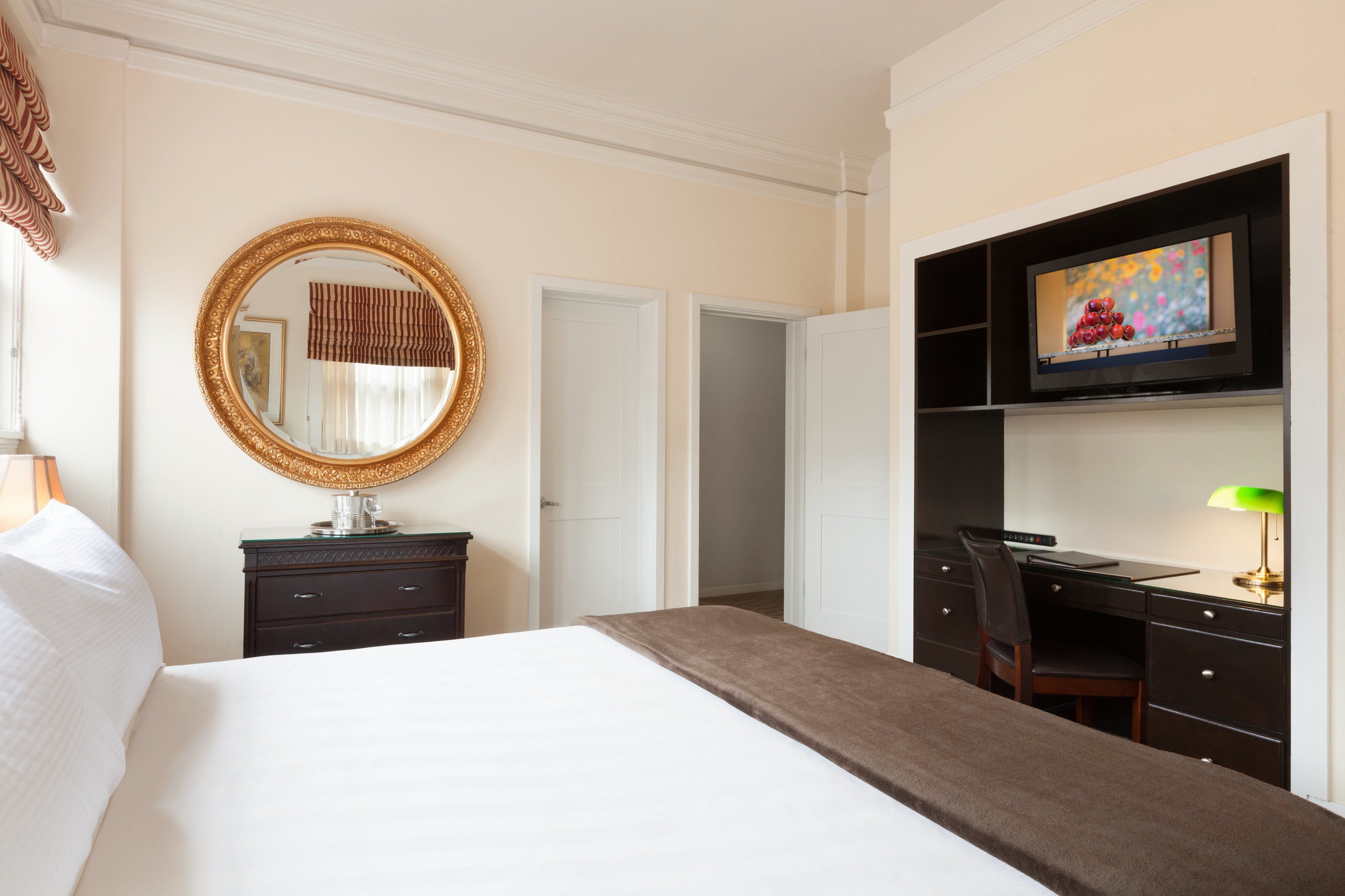 Una habitación de hotel con una cama grande, un escritorio con silla, un televisor y un armario.