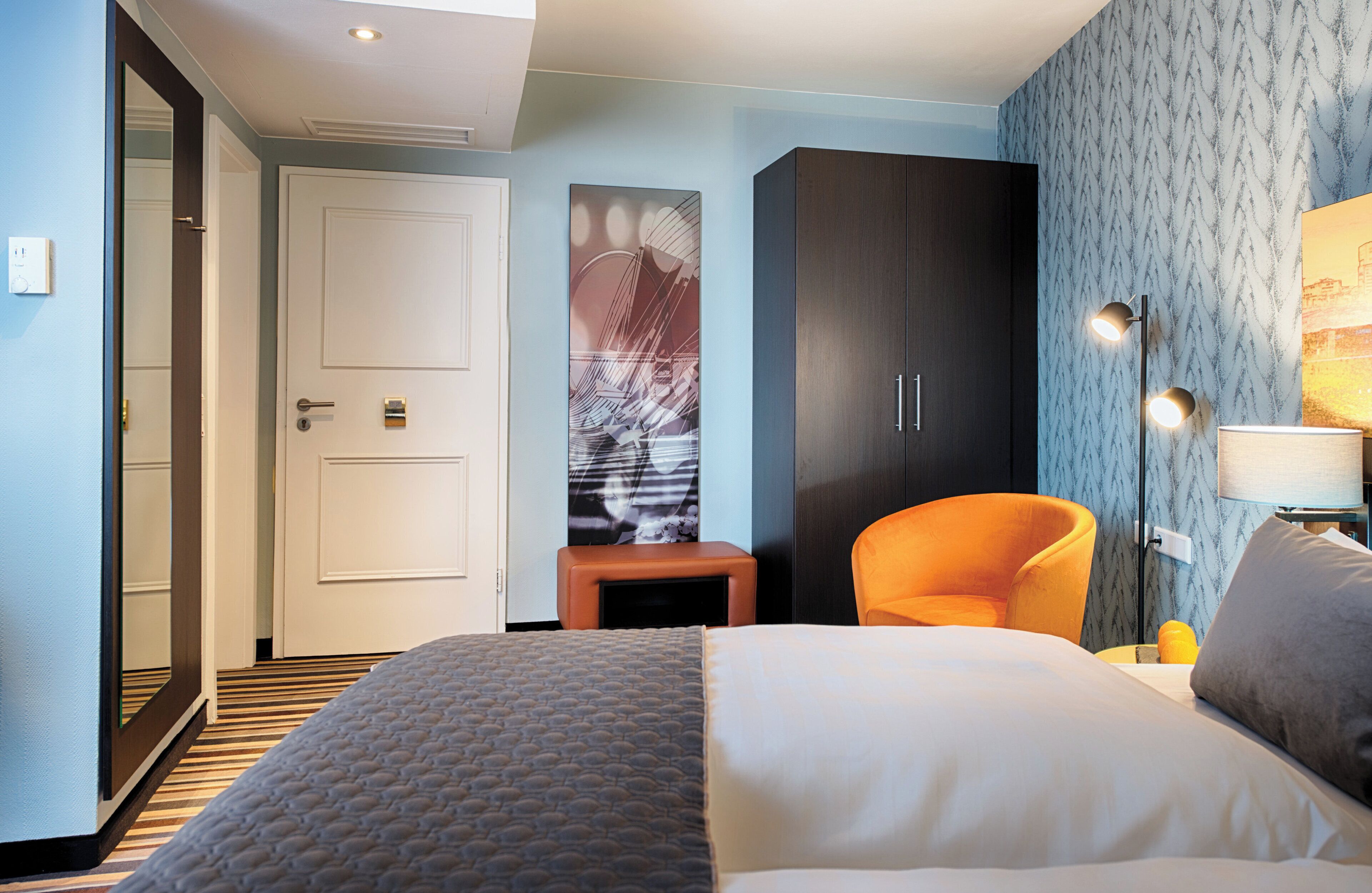 Una habitación de hotel con cama, una silla, un armario y un escritorio.
