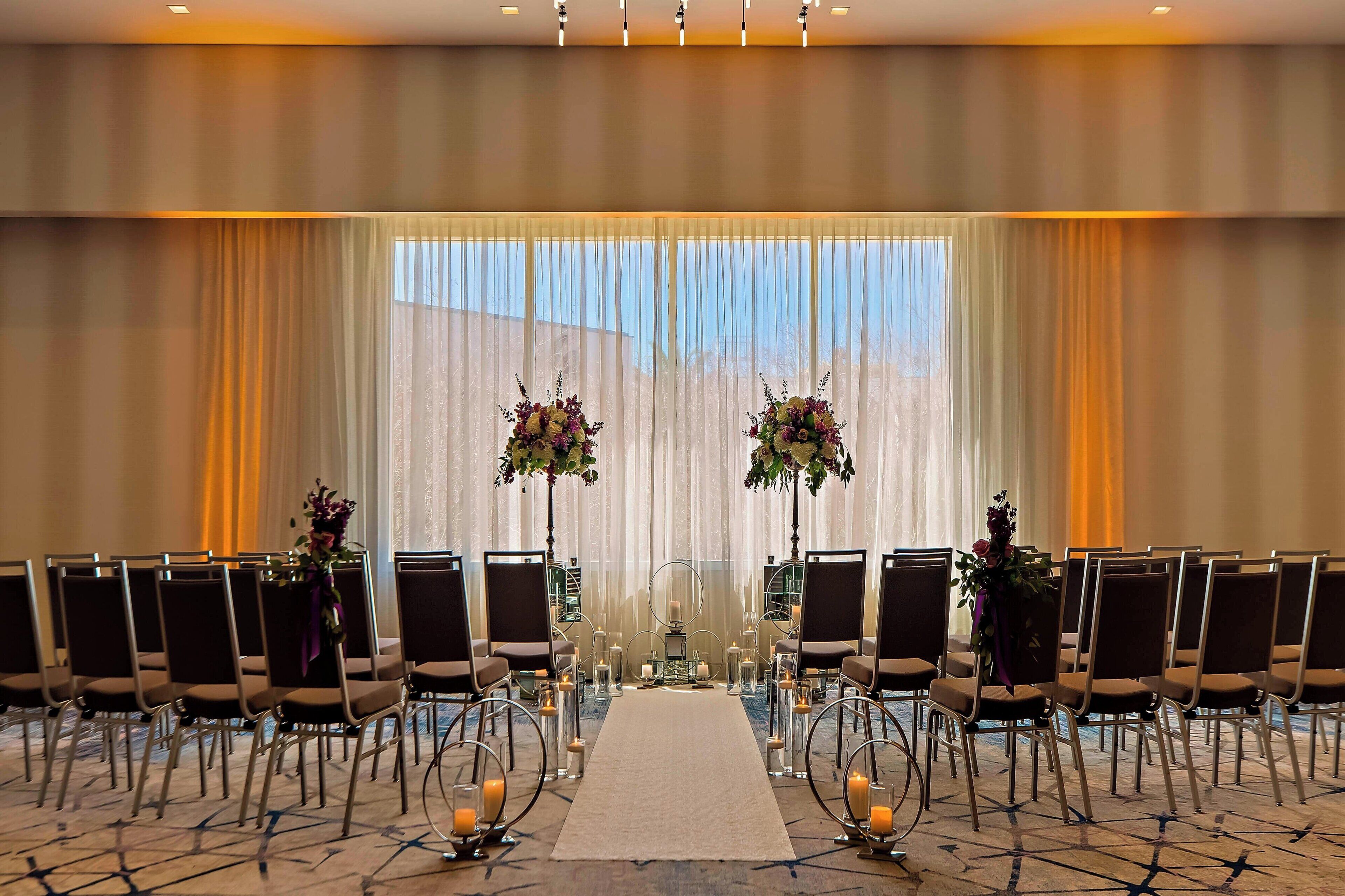 Une salle de conférence avec des rangées de chaises, une allée centrale et des compositions florales.
