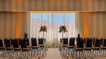 Une salle de conférence avec des rangées de chaises, une allée centrale et des compositions florales.