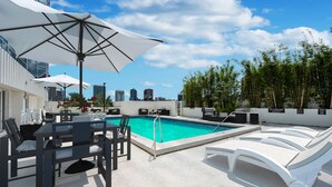 Zona de piscina en la azotea con sillones de descanso, sombrillas y el horizonte de la ciudad al fondo.
