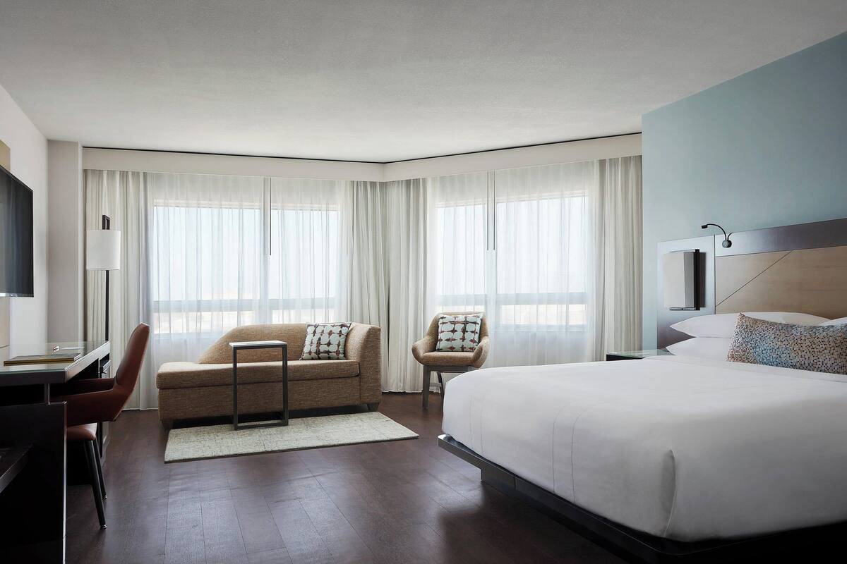 A modern hotel room with a large bed, a sofa, a chair, a desk, and a TV.