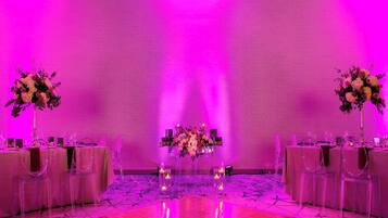 Una habitación con una larga mesa dispuesta para un evento formal, sillas traslúcidas y un centro de mesa floral.