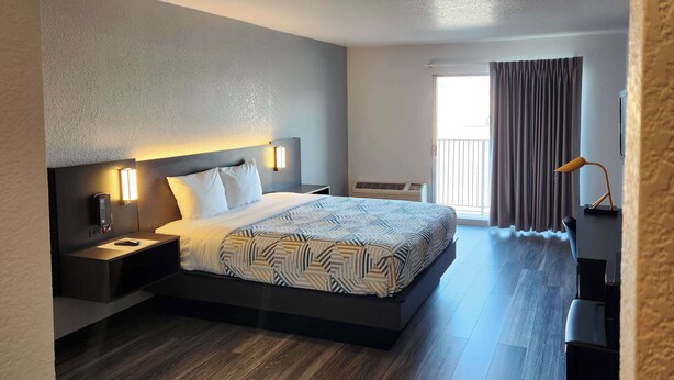 A modern hotel room with a large bed, bedside tables, a desk, and a window with curtains. - Motel 6 Lincoln, NE - Airport (Lincoln)