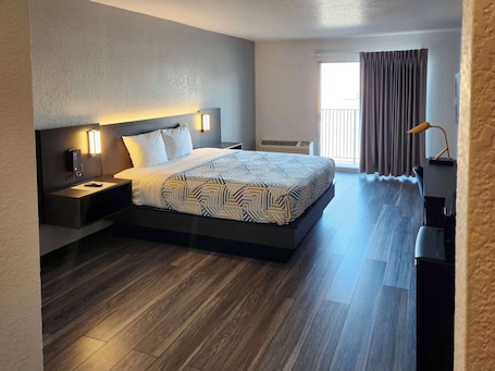 A modern hotel room with a large bed, bedside tables, a desk, and a window with curtains.