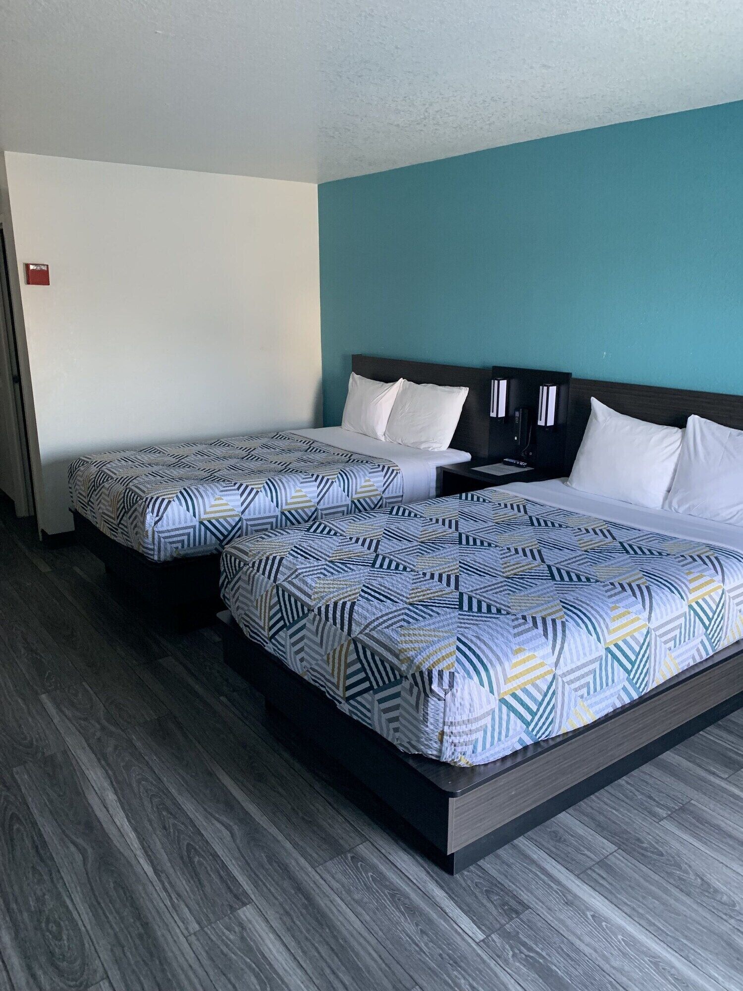 A hotel room with two beds, a dark headboard, and a teal accent wall.