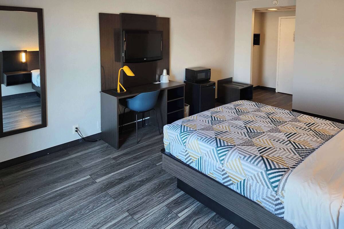 A hotel room with a bed, a desk with a chair, a TV, a microwave, and a small refrigerator.