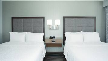 A hotel room with two beds, a nightstand with a lamp, and a wall-mounted panel.