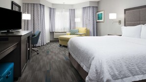 A hotel room with a bed, a desk with a TV, a chair, a lamp, and a window with curtains. - Hampton Inn Monterey (Monterey)