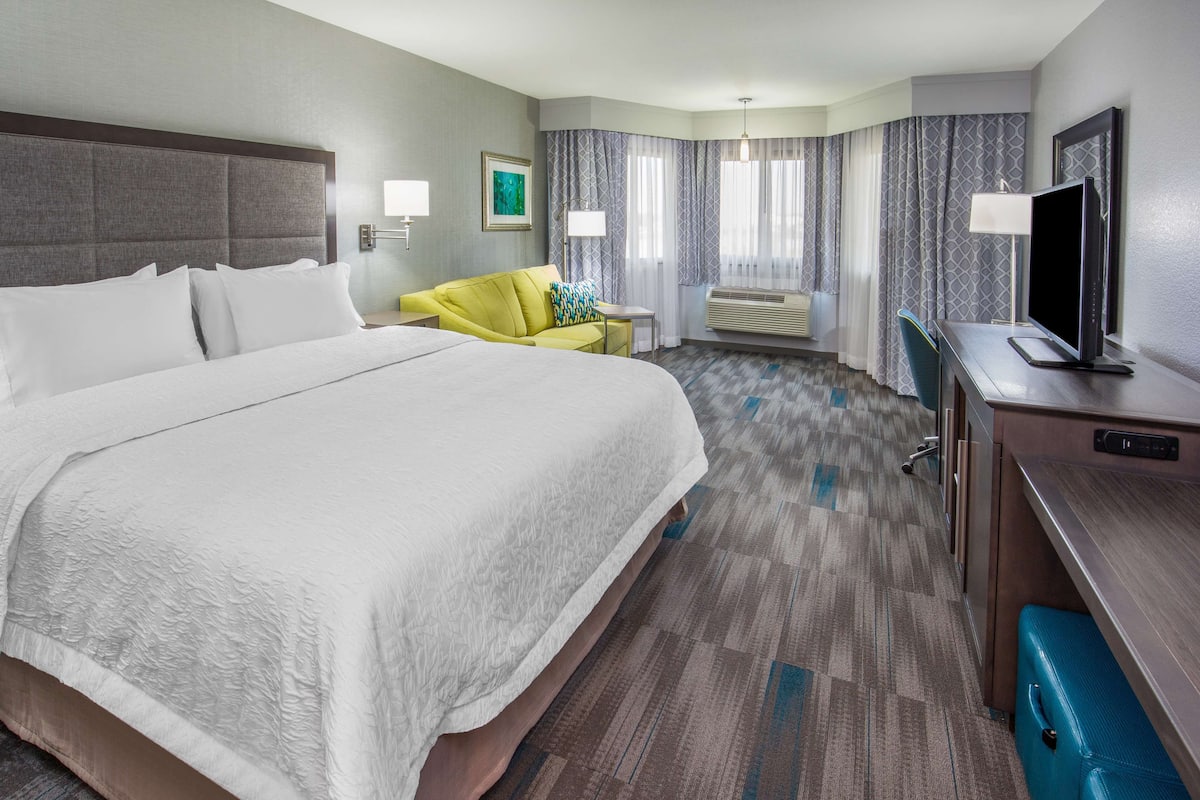 Ein Hotelzimmer mit einem großen Bett, einem Schreibtisch, einem Flachbildfernseher, einem Sessel und einem kleinen Tisch.