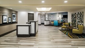 A hotel lobby with a reception desk, seating area, and a large wall with framed pictures. - Hampton Inn Monterey (Monterey)
