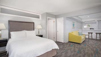 Una habitación de hotel con una cama grande, un sofá amarillo, una pequeña cocina y un baño independiente.