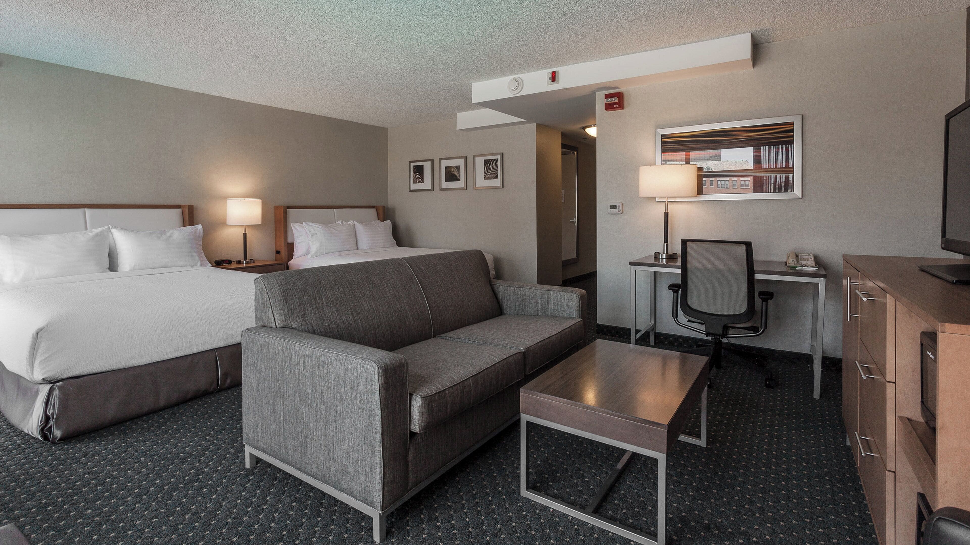 A hotel room with a bed, a sofa, a desk, and a television.