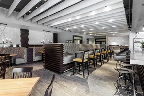 A modern restaurant interior with high ceilings, exposed beams, and a mix of seating arrangements including booths and tables. - Holiday Inn Chicago North-Evanston by IHG (Evanston)