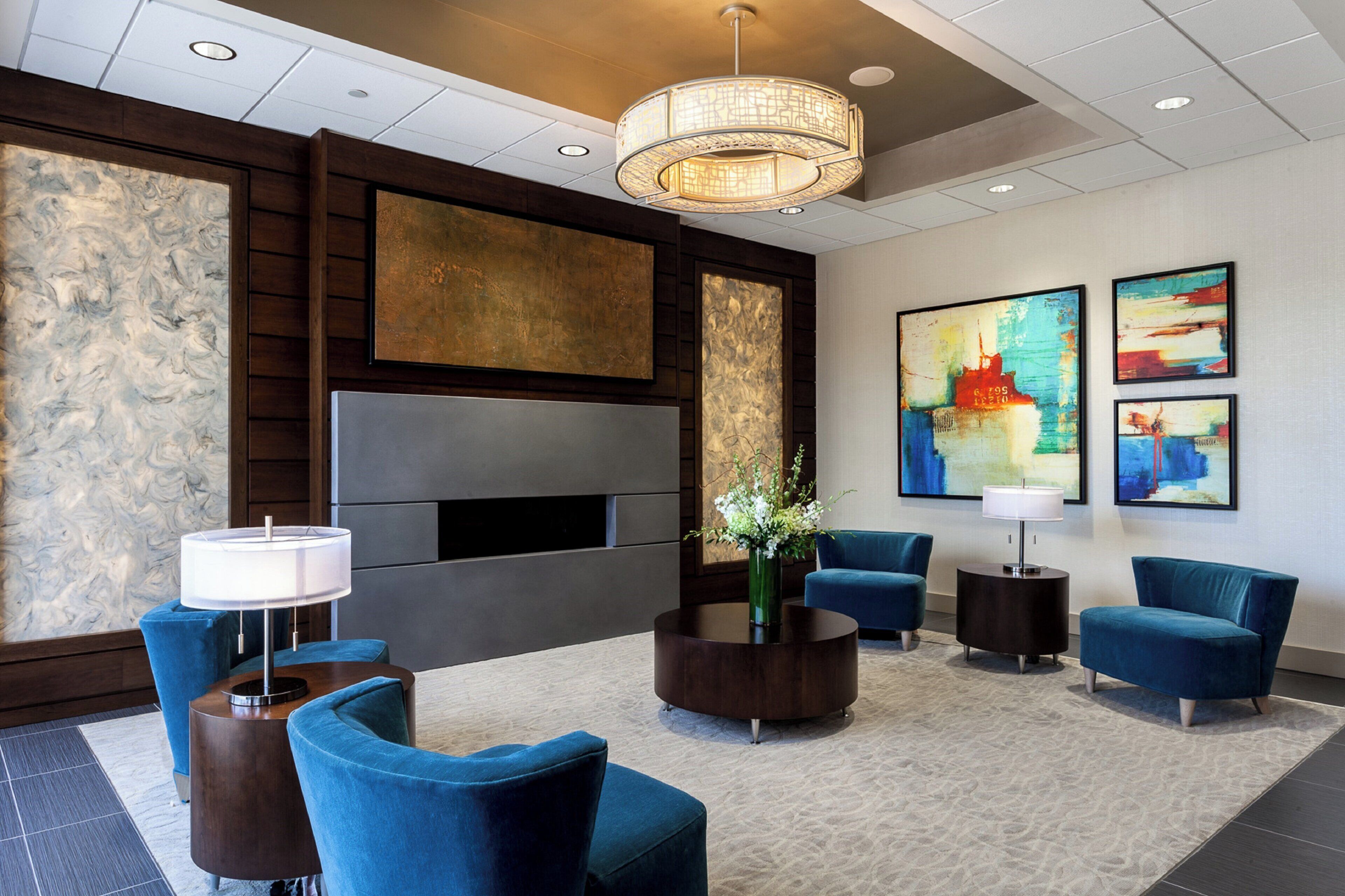 A lobby with a seating area, a large flat-screen TV, artwork on the walls, and a chandelier.