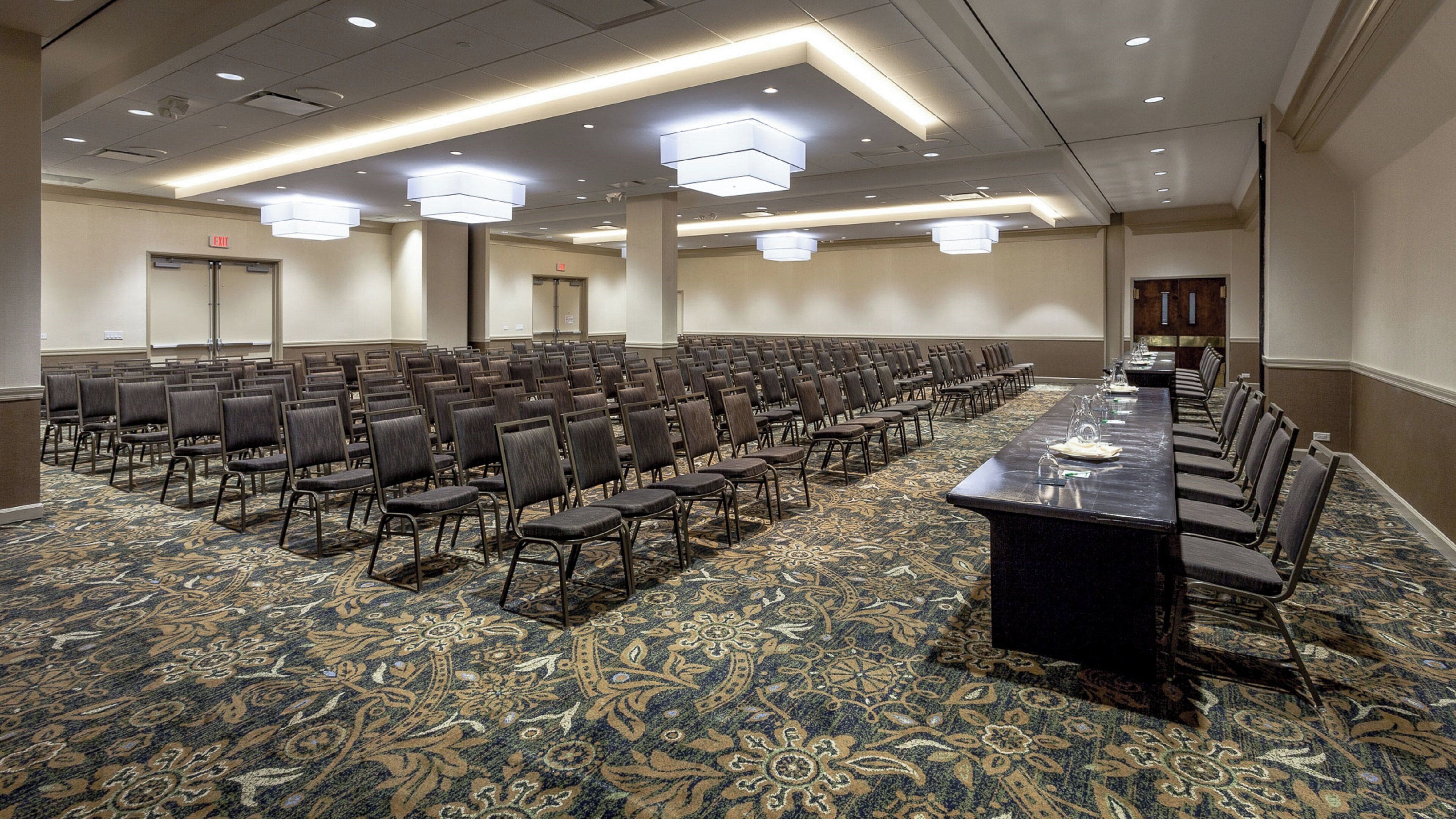 A conference room with rows of chairs, a long table, and a patterned carpet.