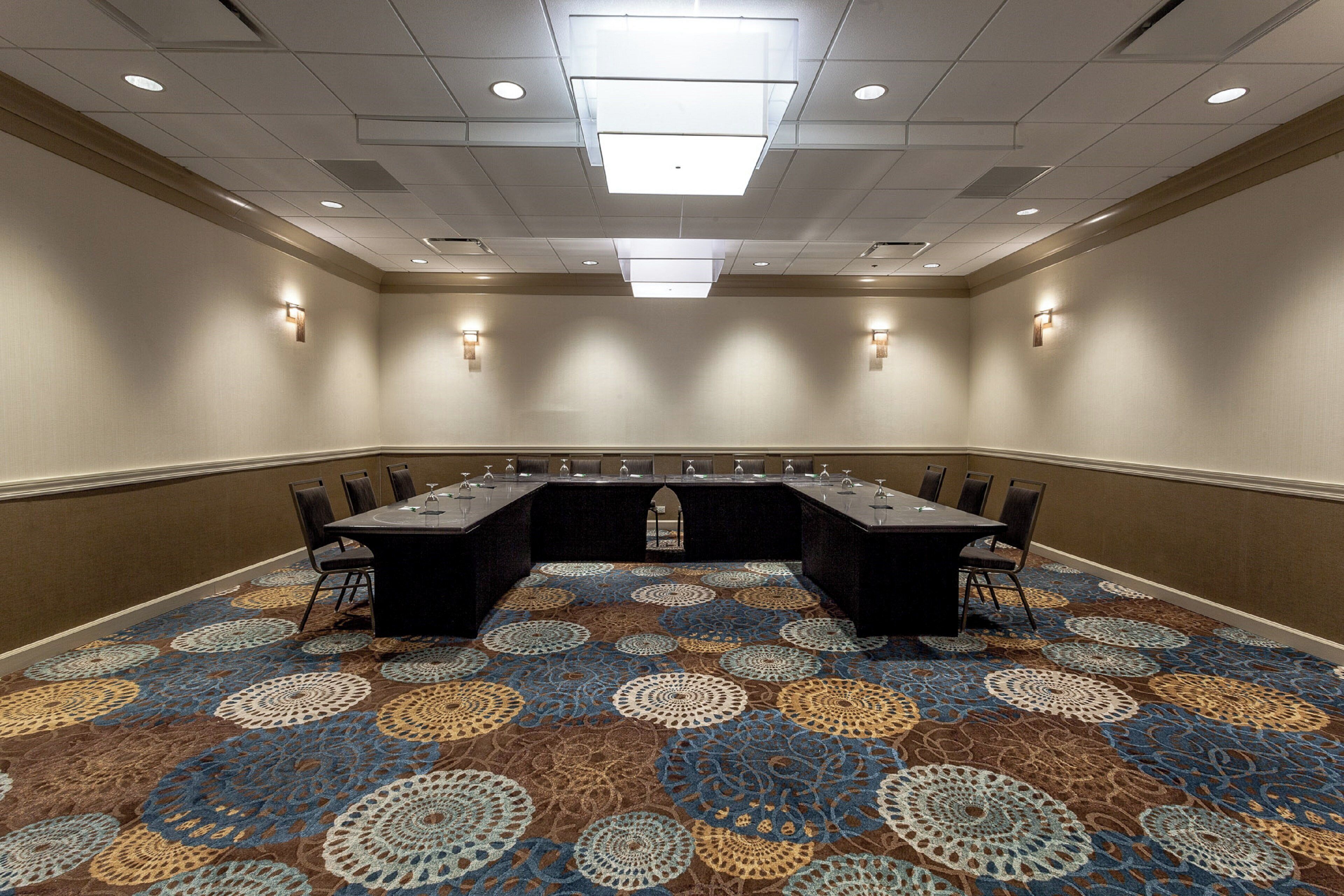 A conference room with a long table, chairs, and a patterned carpet.