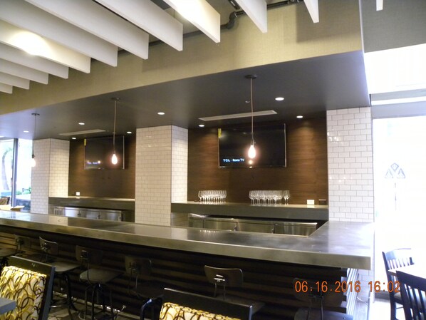 A modern bar area with a long counter, multiple seating options, and a flat-screen TV mounted on the wall. - Holiday Inn Chicago North-Evanston by IHG (Evanston)