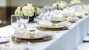 A long table set with white plates, gold cutlery, and clear wine glasses, with a bouquet of flowers in the background.