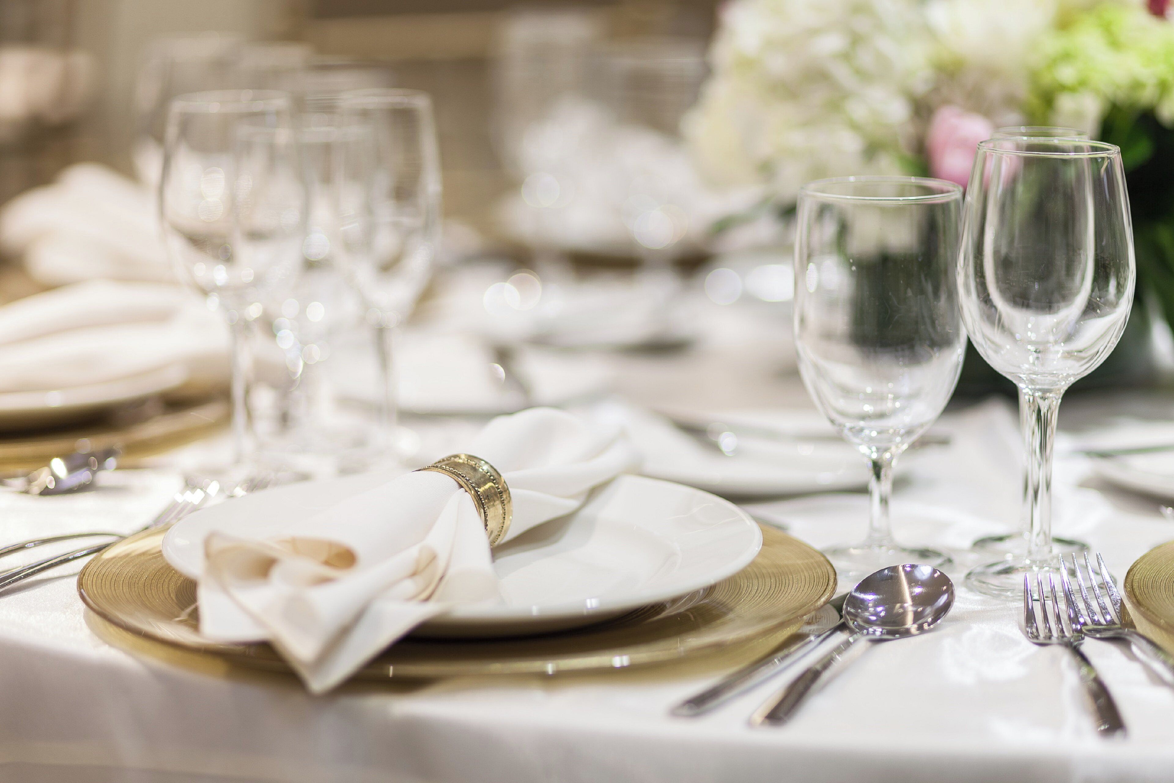 A table set with white plates, gold cutlery, and clear wine glasses, indicating a formal dining arrangement.