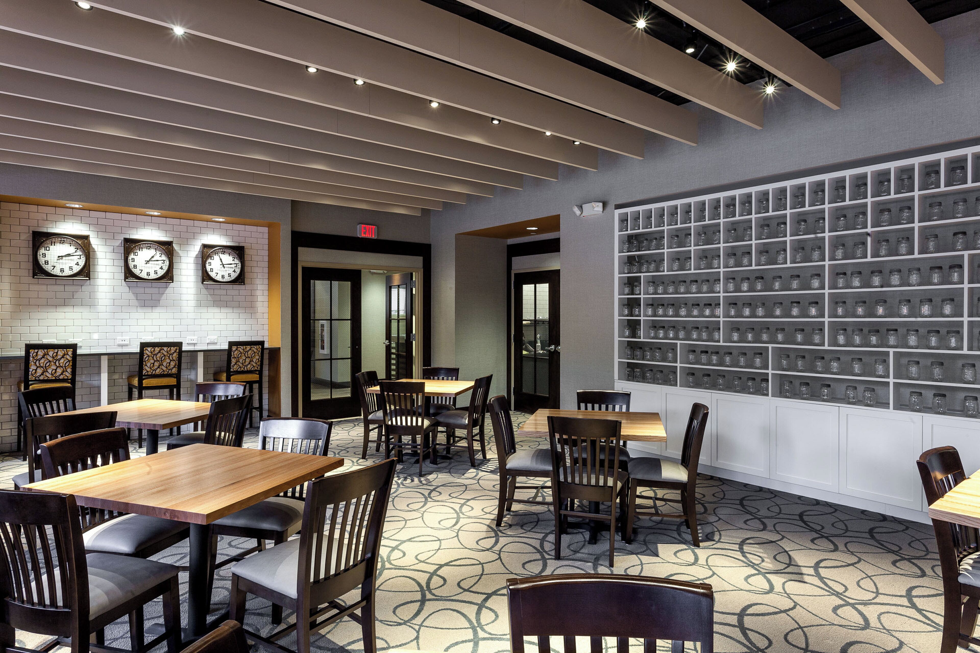 A restaurant interior with multiple tables and chairs, a wall of hanging jars, and clocks on the wall.