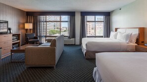 A hotel room with two beds, a desk, a chair, a TV, and a view of the cityscape.
