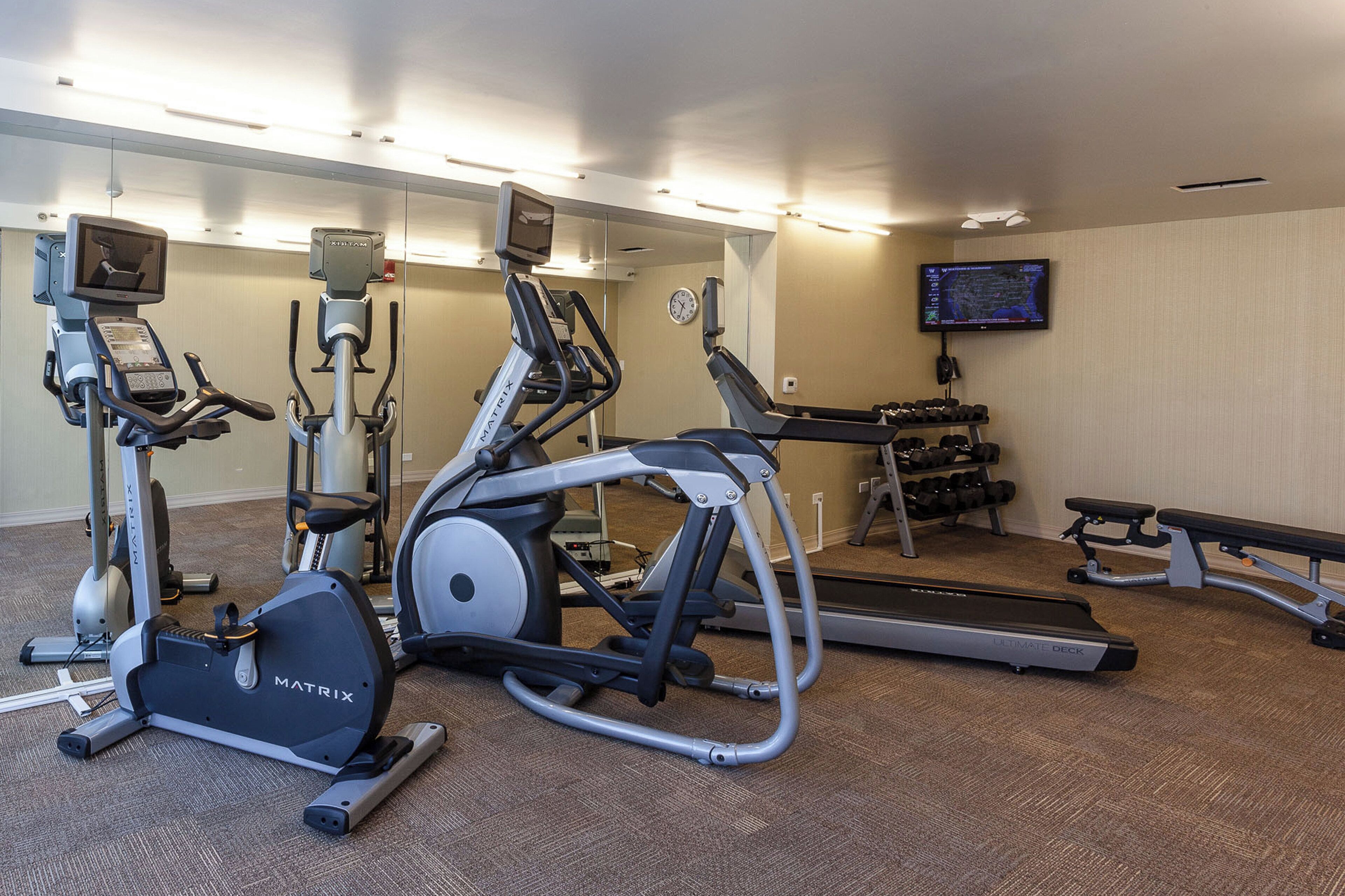 Une salle de sport équipée de divers appareils d’exercice, notamment des tapis de course, des vélos d’appartement et des appareils de musculation.
