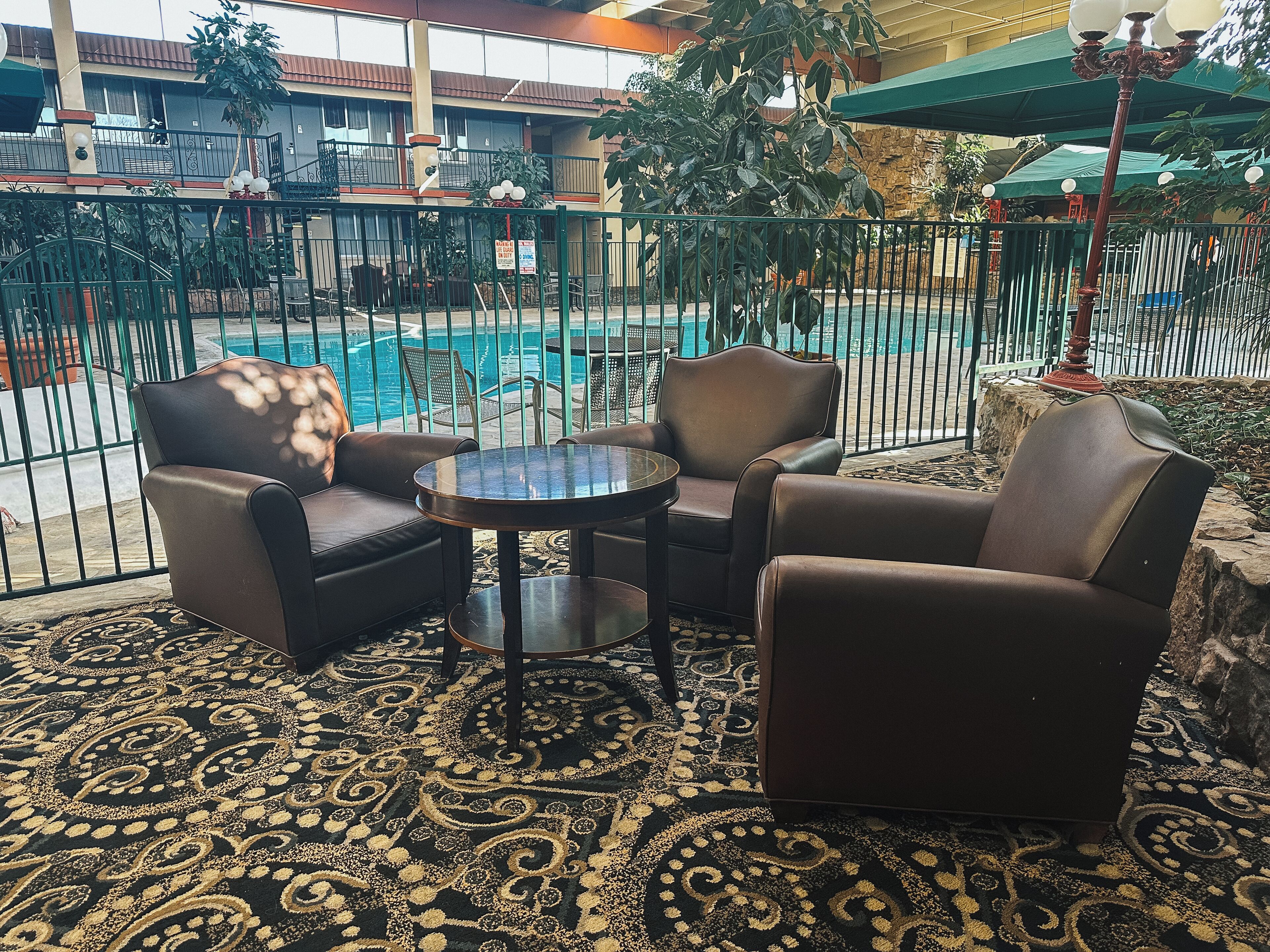 A balcony with a pool view, furnished with leather chairs and a small table, featuring a patterned carpet.