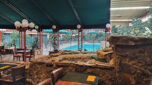 An indoor dining area with stone walls, wooden tables, and chairs. There is a view of a swimming pool and greenery outside. - Clarion Inn (Fort Collins)