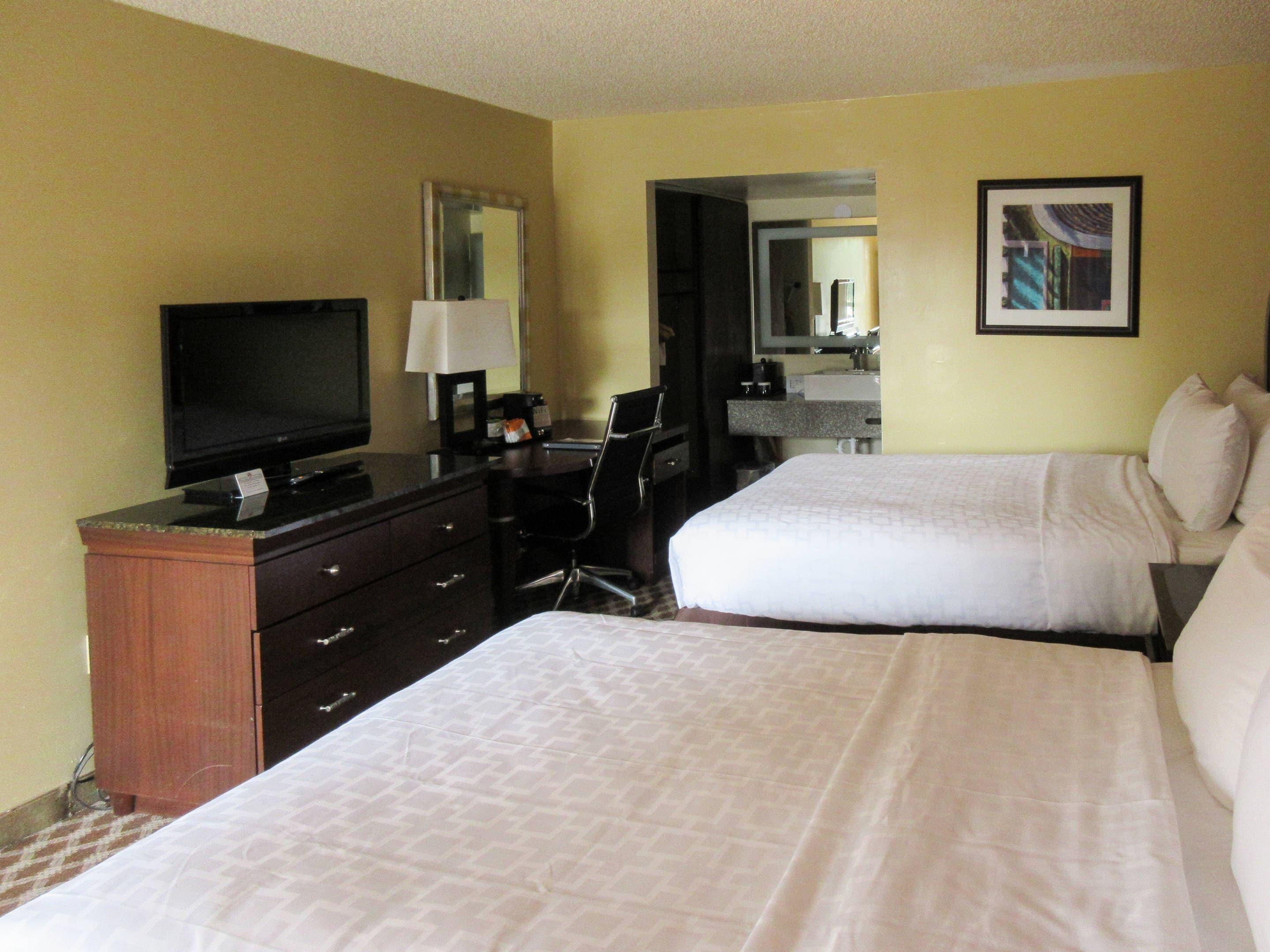 A hotel room with two beds, a desk, a television, and a bathroom visible through an open door.